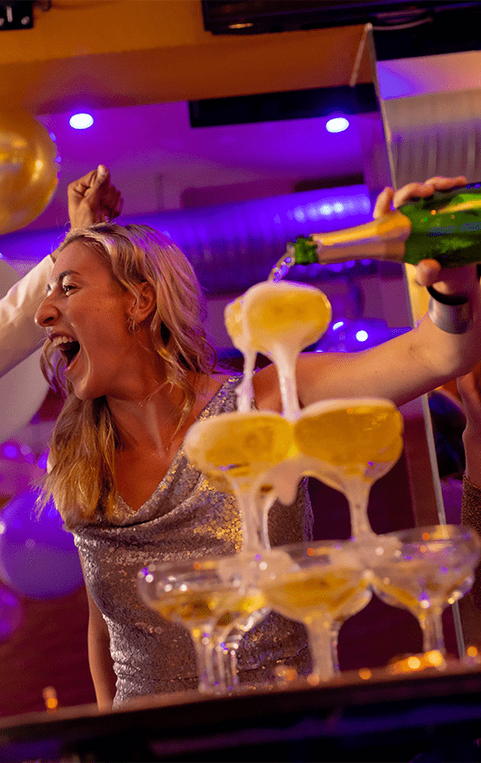 Woman pouring champagne into a glass tower at a celebration.