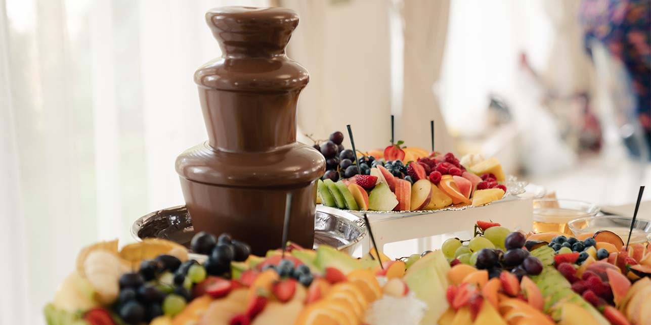 Chocolate fountain with skewered fruit displayed around the base.