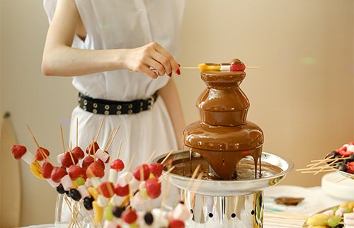 Chocolate fountain with strawberries on skewers being dipped.