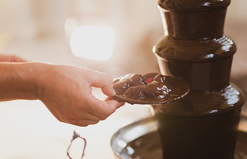 Hand holding plate while scooping chocolate from a fountain.