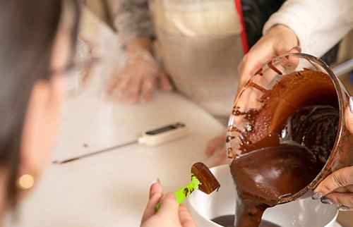 Person dipping fruit into a chocolate fountain at an event.