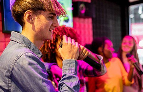 Man singing karaoke into a mic at a lively party.